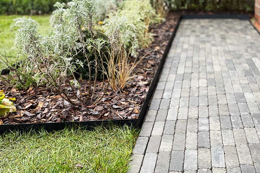 metal garden edging used to separate a garden border, lawn and block paved path 